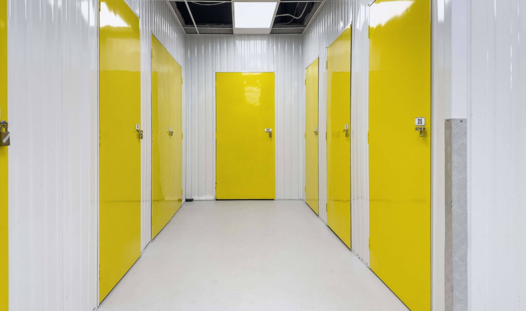 A clean and well-lit hallway of modern indoor storage units, featuring vibrant yellow doors and secure locking mechanisms.